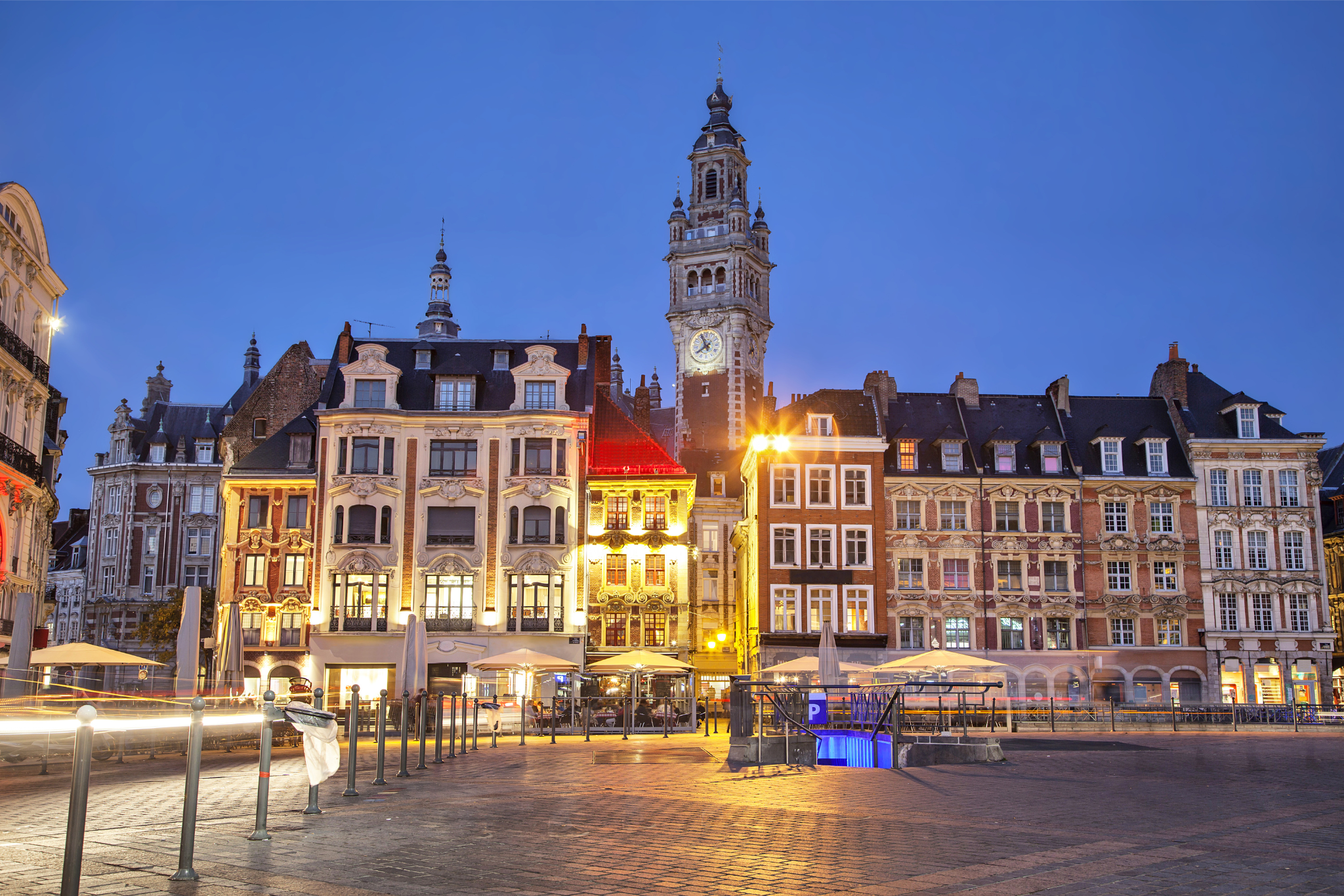 Place de ville illuminée avec bâtiments historiques et tour d’horloge de nuit